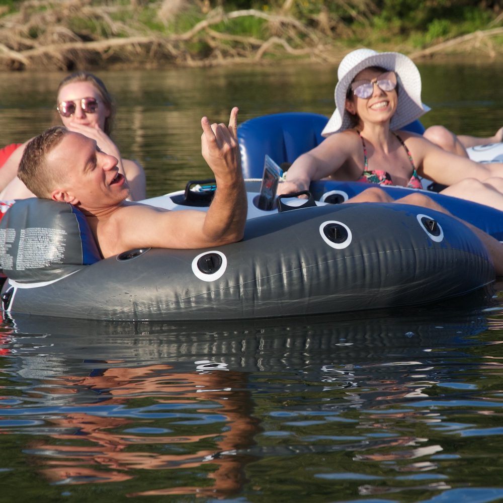 Three people recline in innertubes, floating on lake